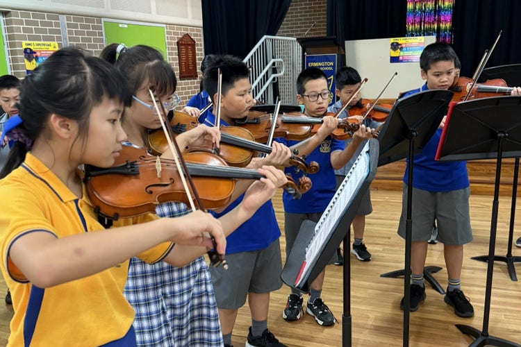 six students playing their violins in the school's hall